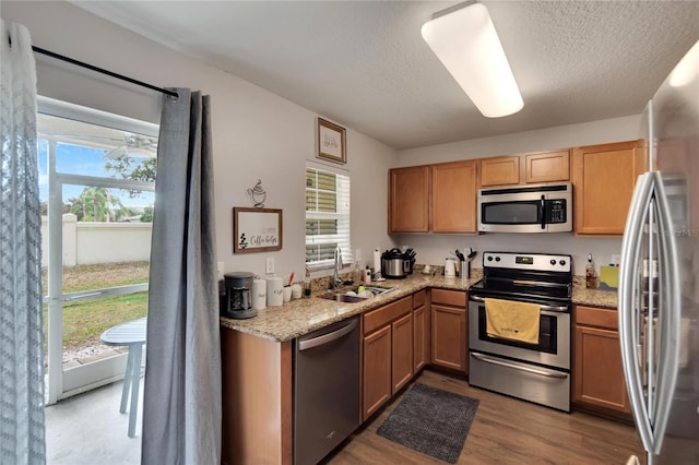 kitchen with appliances with stainless steel finishes, light stone counters, a textured ceiling, sink, and light hardwood / wood-style floors