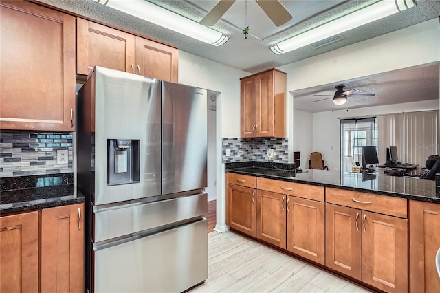 kitchen featuring ceiling fan, backsplash, light hardwood / wood-style flooring, dark stone countertops, and stainless steel fridge