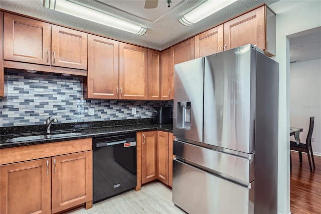 kitchen featuring stainless steel fridge, black dishwasher, sink, light hardwood / wood-style floors, and dark stone countertops