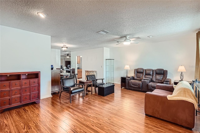 living room featuring ceiling fan, a textured ceiling, and light wood-type flooring