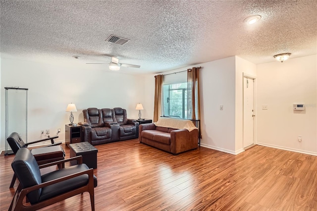 living room featuring light wood-type flooring, a textured ceiling, and ceiling fan