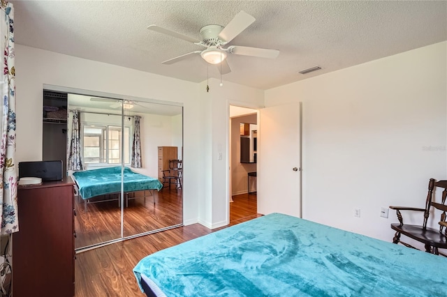 bedroom with a textured ceiling, dark wood-type flooring, ceiling fan, and a closet