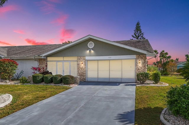 view of front facade with a front yard, stone siding, driveway, and an attached garage