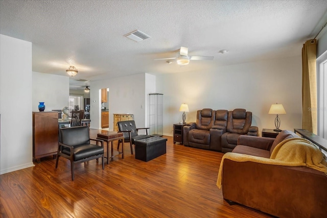 living area featuring ceiling fan, a textured ceiling, wood finished floors, and visible vents