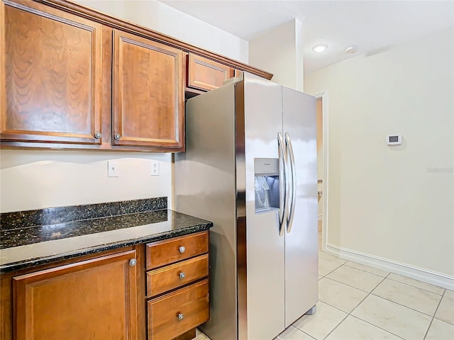 kitchen with dark stone countertops, stainless steel fridge with ice dispenser, and light tile patterned flooring