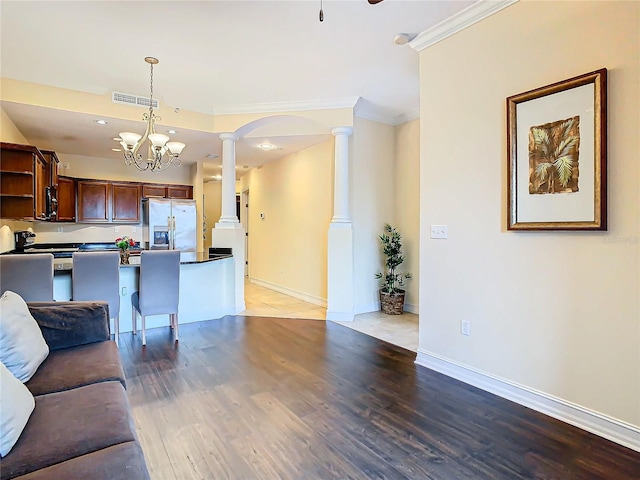 unfurnished living room with hardwood / wood-style floors, an inviting chandelier, crown molding, and decorative columns