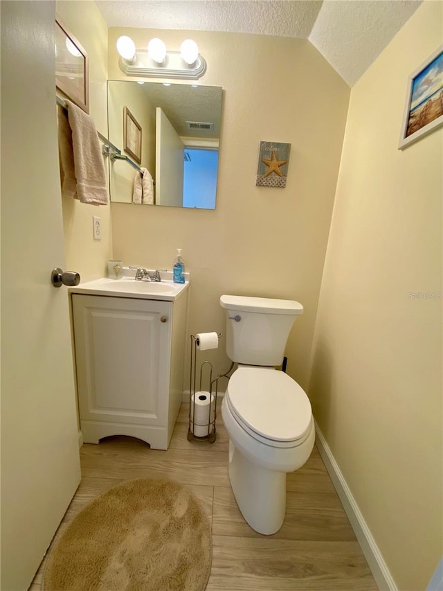 bathroom with a textured ceiling, vanity, vaulted ceiling, hardwood / wood-style flooring, and toilet