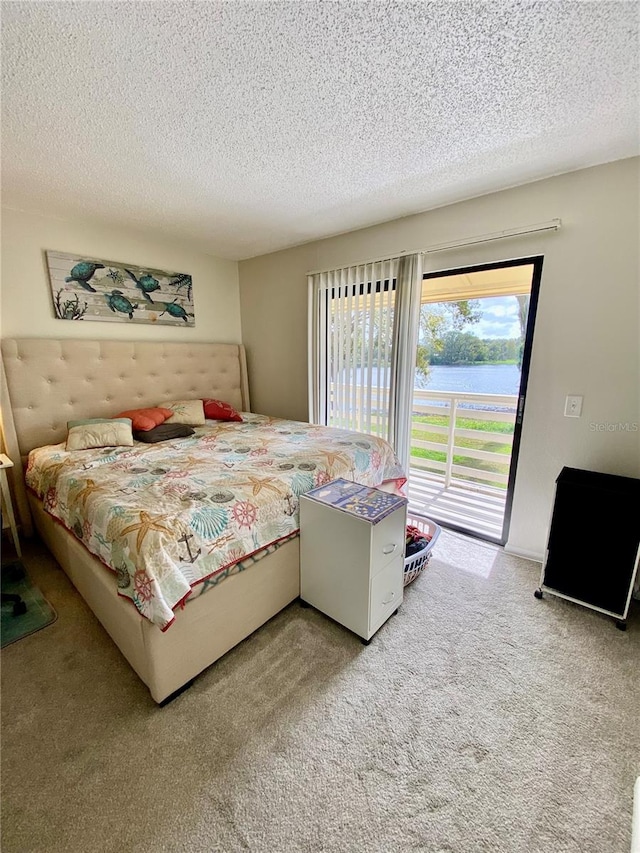 carpeted bedroom featuring access to exterior, a textured ceiling, and a water view