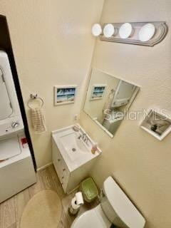 bathroom with hardwood / wood-style floors, stacked washer / drying machine, and toilet