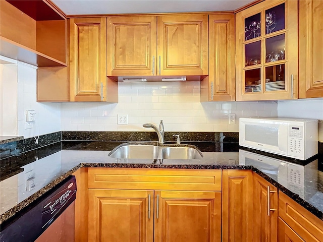 kitchen with dark stone countertops, stainless steel dishwasher, sink, and backsplash