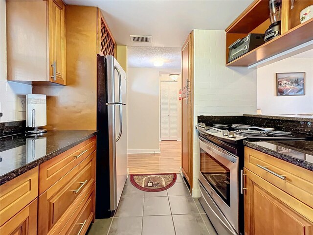 kitchen featuring stainless steel appliances, a textured ceiling, light tile patterned floors, decorative backsplash, and dark stone countertops