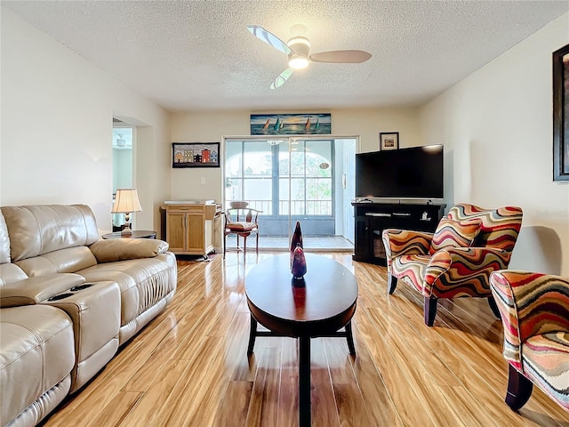 living room featuring ceiling fan, a textured ceiling, and light hardwood / wood-style flooring