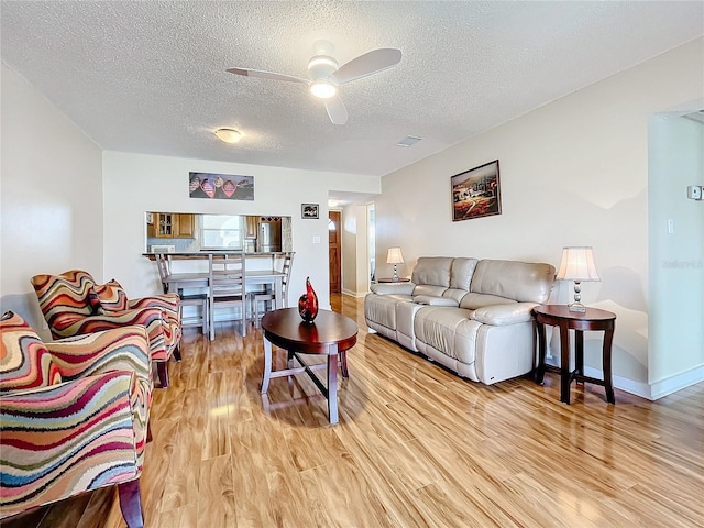 living room with light hardwood / wood-style floors, ceiling fan, and a textured ceiling