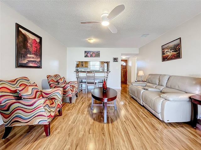 living room with a textured ceiling, ceiling fan, and light hardwood / wood-style flooring