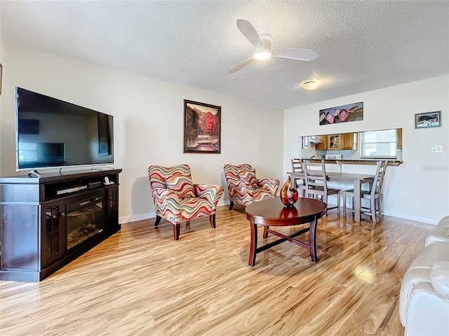 living room featuring light hardwood / wood-style flooring, a textured ceiling, and ceiling fan