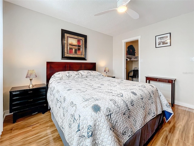 bedroom with ceiling fan, a textured ceiling, a spacious closet, light hardwood / wood-style flooring, and a closet