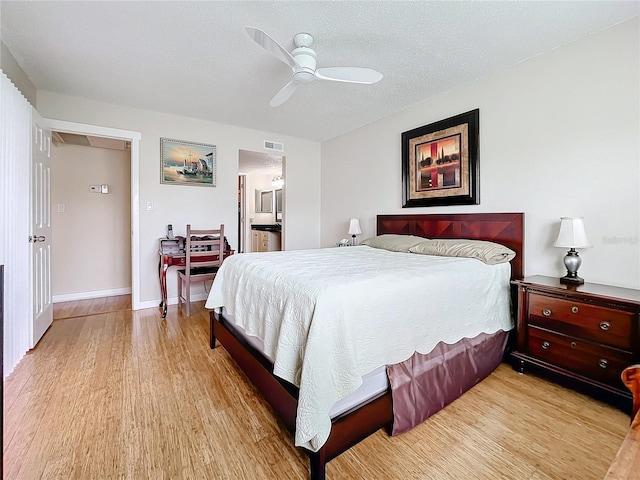 bedroom featuring ceiling fan, connected bathroom, light wood-type flooring, and a textured ceiling