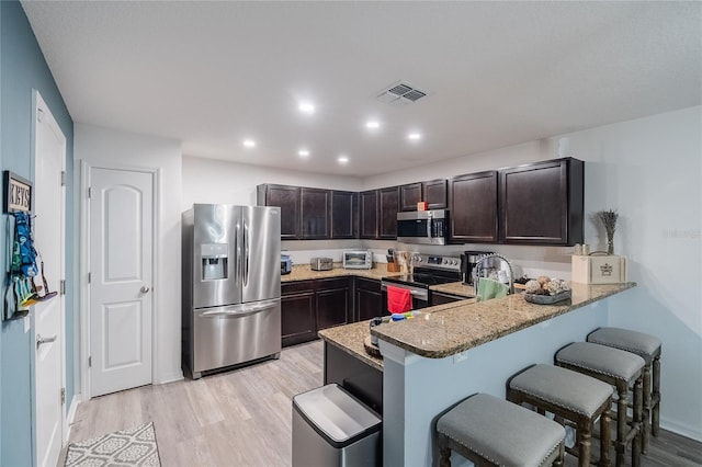 kitchen featuring light wood-type flooring, kitchen peninsula, light stone counters, and stainless steel appliances