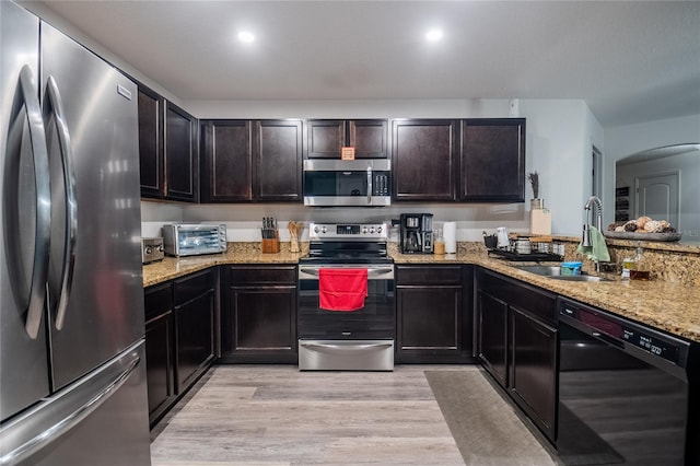 kitchen featuring stainless steel appliances, light wood-type flooring, dark brown cabinetry, light stone countertops, and sink