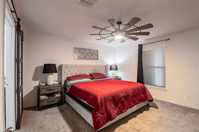 bedroom with a barn door, ceiling fan, and carpet floors