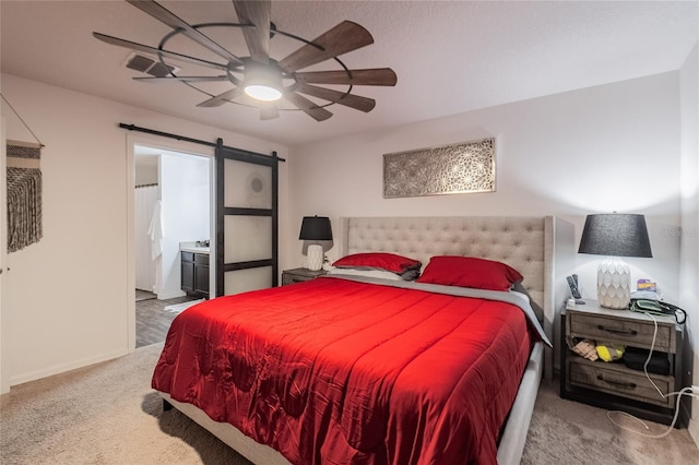 bedroom with ensuite bathroom, light colored carpet, a barn door, and ceiling fan