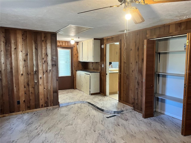 kitchen with a textured ceiling, white cabinetry, wooden walls, and ceiling fan