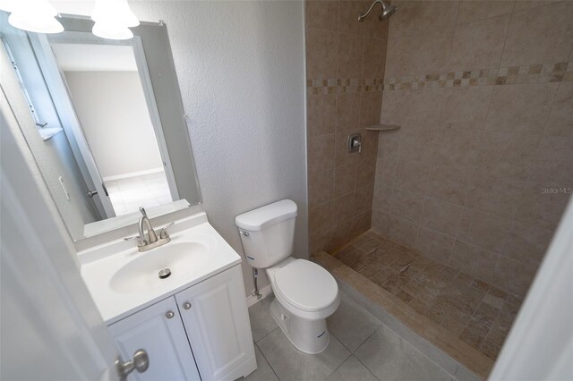 bathroom featuring tile patterned flooring, vanity, tiled shower, and toilet