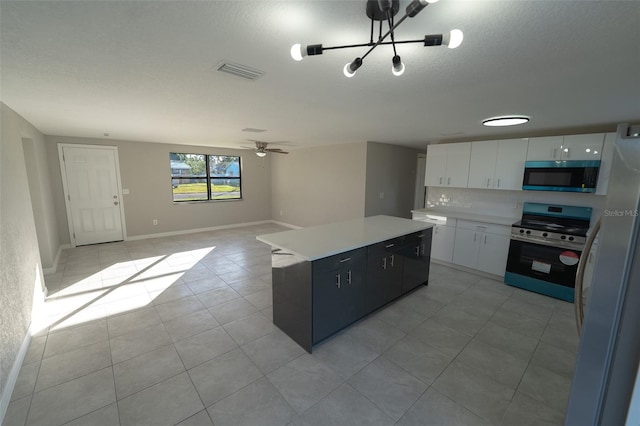 kitchen featuring appliances with stainless steel finishes, ceiling fan with notable chandelier, light tile patterned floors, a center island, and white cabinetry