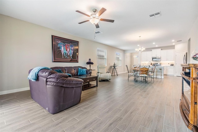 living room featuring ceiling fan with notable chandelier and light hardwood / wood-style flooring