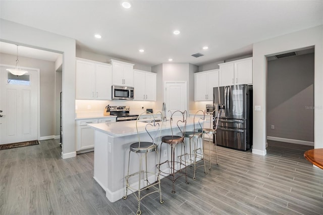 kitchen featuring a center island with sink, light wood-type flooring, appliances with stainless steel finishes, a kitchen bar, and white cabinets