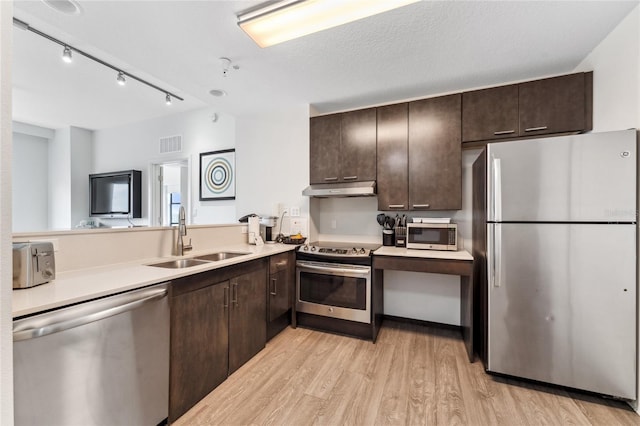 kitchen with stainless steel appliances, light hardwood / wood-style floors, sink, track lighting, and a textured ceiling