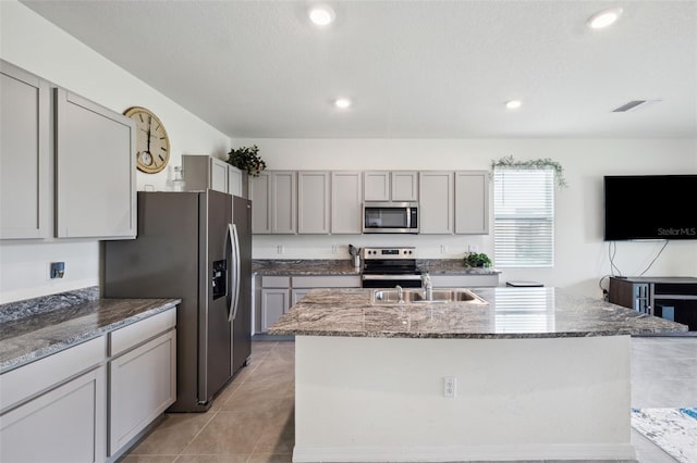 kitchen featuring appliances with stainless steel finishes, gray cabinets, a kitchen island with sink, and sink