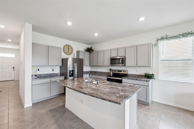 kitchen with sink, a center island with sink, dark stone countertops, appliances with stainless steel finishes, and gray cabinets