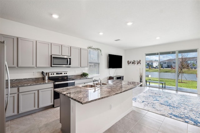 kitchen with appliances with stainless steel finishes, gray cabinets, and a kitchen island with sink