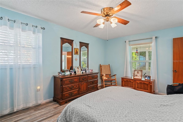 bedroom with a textured ceiling, ceiling fan, light hardwood / wood-style flooring, and multiple windows