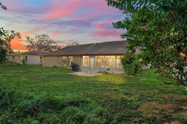 back house at dusk with a patio area and a lawn