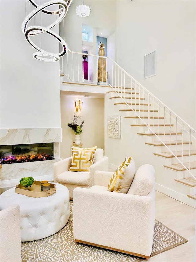 living room featuring a high end fireplace, wood-type flooring, a notable chandelier, and a high ceiling