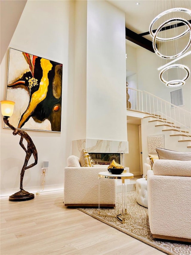 living room with a towering ceiling, a high end fireplace, wood-type flooring, and an inviting chandelier