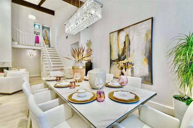 dining area with beamed ceiling, a towering ceiling, an inviting chandelier, and light hardwood / wood-style flooring