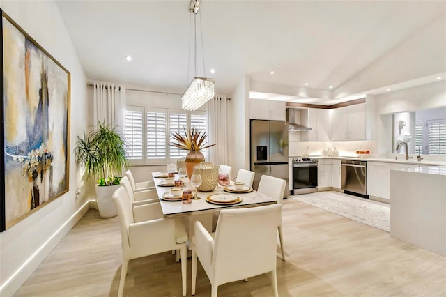 dining area with sink, lofted ceiling, and light wood-type flooring