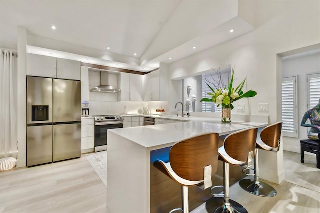 kitchen featuring a breakfast bar area, kitchen peninsula, wall chimney range hood, and appliances with stainless steel finishes