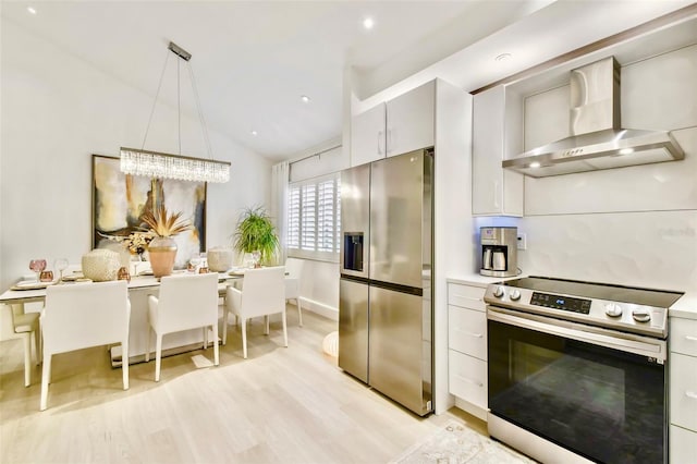 kitchen featuring appliances with stainless steel finishes, light wood-type flooring, vaulted ceiling, wall chimney range hood, and pendant lighting