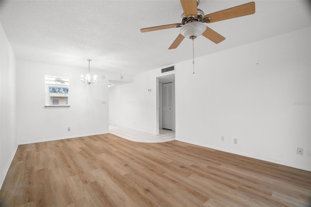 empty room featuring a textured ceiling, light wood finished floors, ceiling fan with notable chandelier, and visible vents