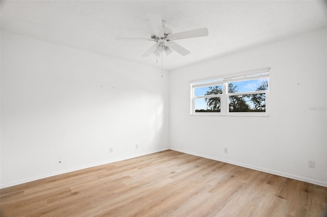 empty room with a textured ceiling, a ceiling fan, light wood-style flooring, and baseboards