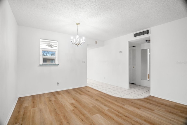 spare room with an inviting chandelier, a textured ceiling, visible vents, and wood finished floors