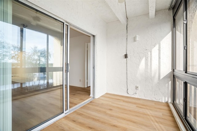 unfurnished room featuring a textured wall, light wood finished floors, and beamed ceiling