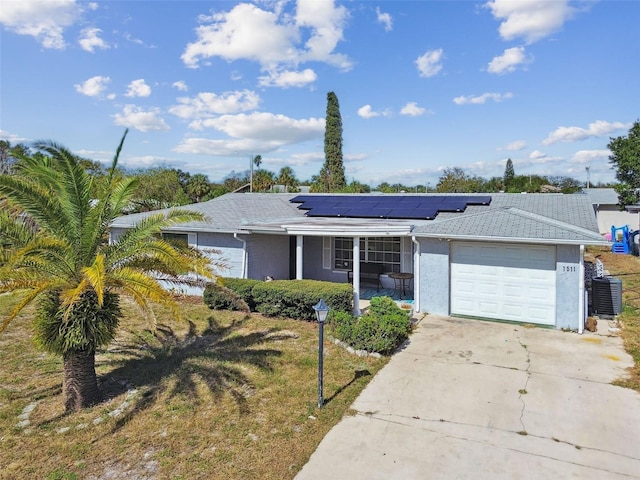 ranch-style home with central air condition unit, a garage, solar panels, and a front yard