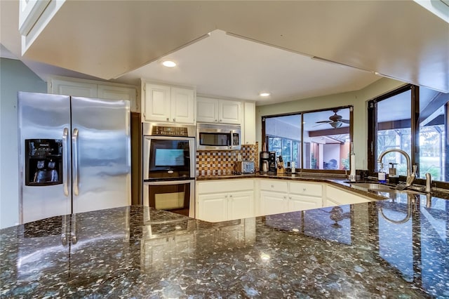 kitchen with stainless steel appliances, dark stone countertops, white cabinetry, and a healthy amount of sunlight