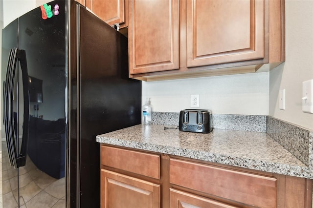 kitchen featuring black fridge, tile patterned floors, and light stone countertops