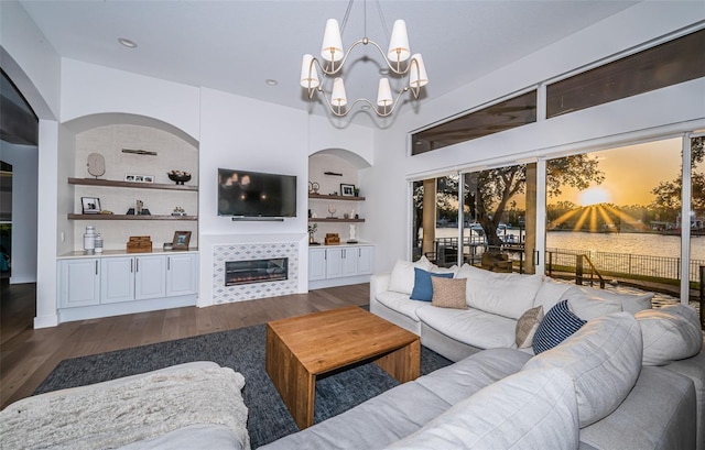 living room with built in shelves, a fireplace, dark hardwood / wood-style flooring, and a notable chandelier